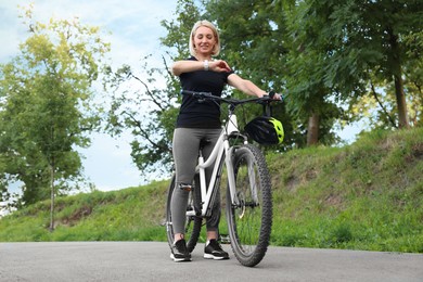 Happy woman on bicycle checking time in park, low angle view