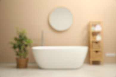 Photo of Blurred view of bathtub, houseplant, shelving unit and mirror in stylish bathroom