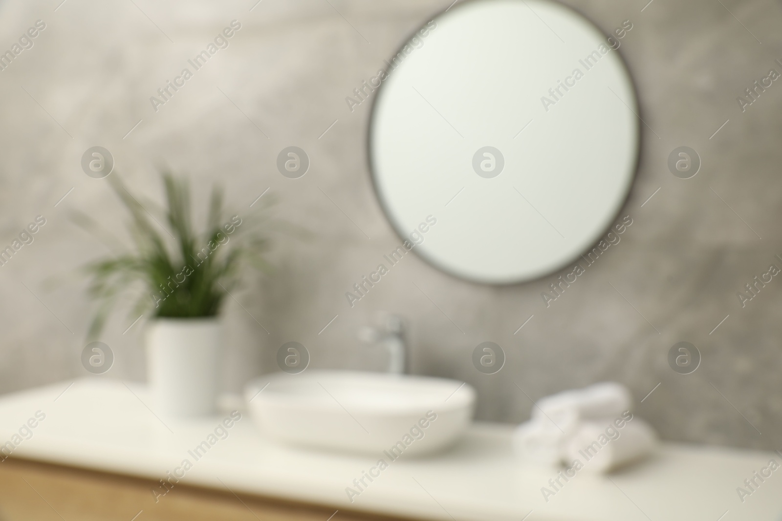 Photo of Blurred view of countertop with sink, towels, houseplant and mirror in bathroom