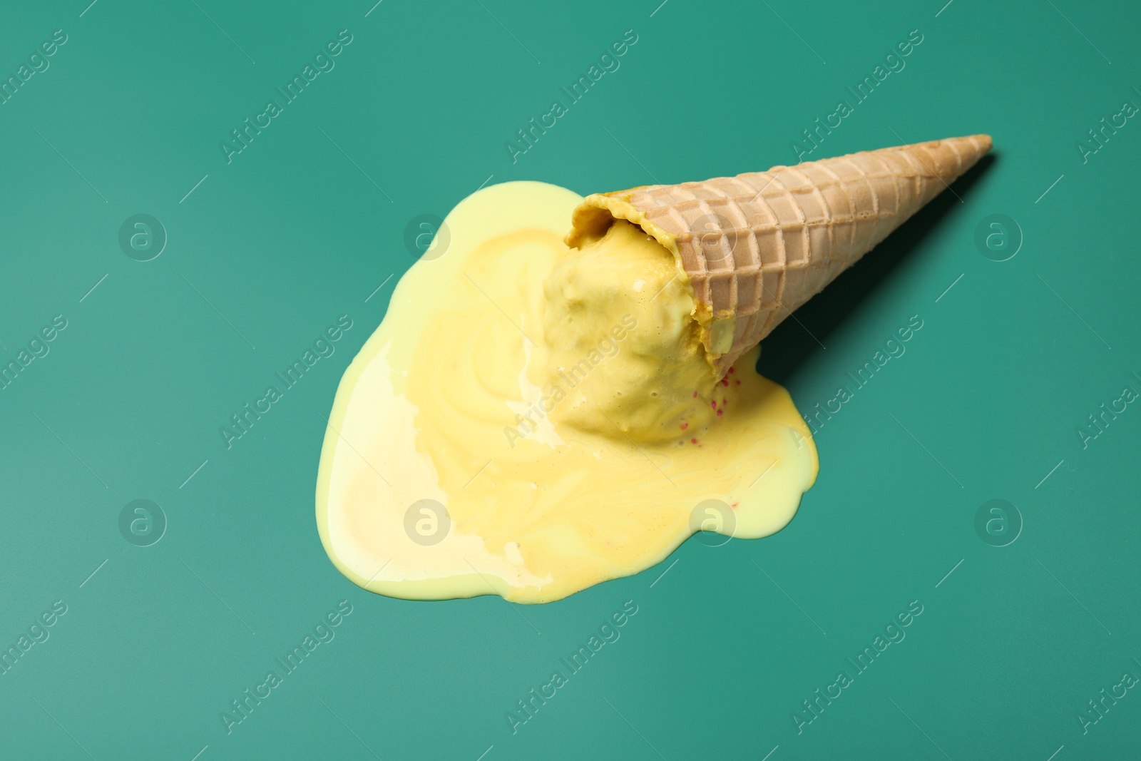 Photo of Melted ice cream in wafer cone on pale green background, top view