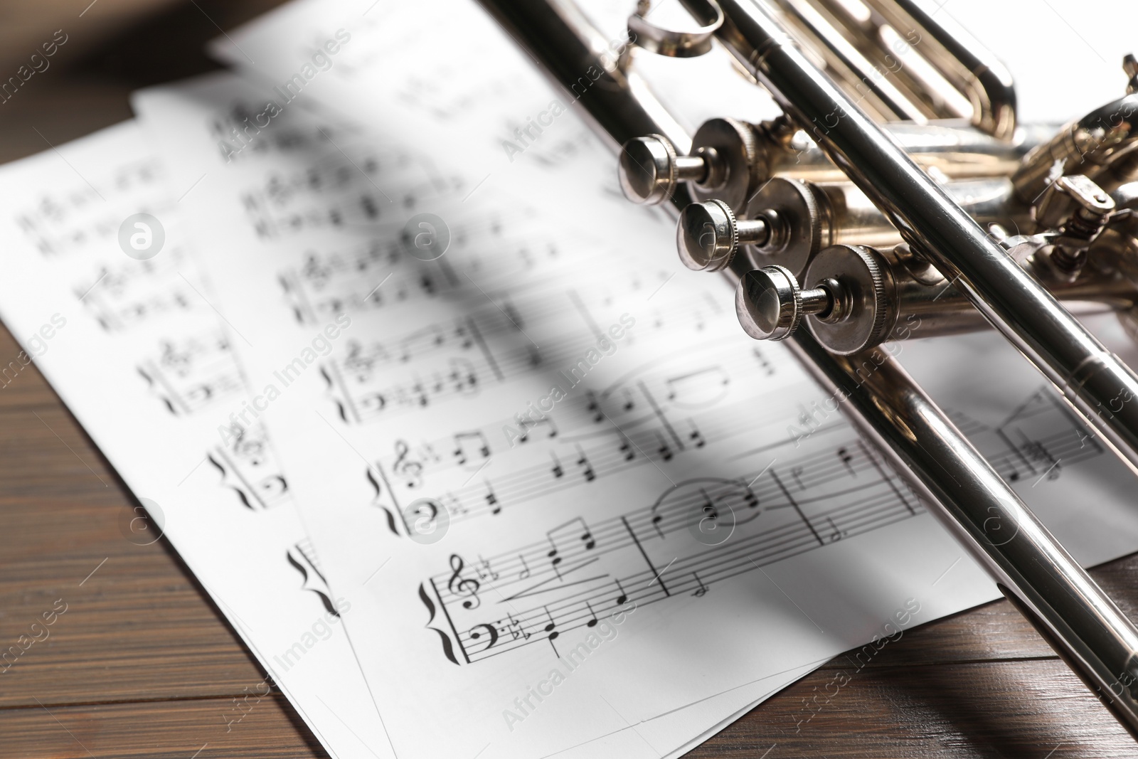 Photo of Trumpet and music sheet papers with notes on wooden table, closeup