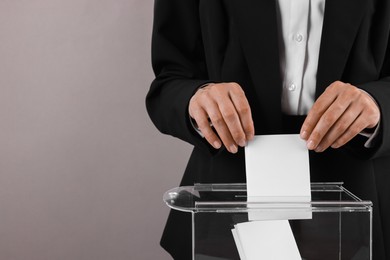 Woman putting her vote into ballot box against grey background, closeup. Space for text