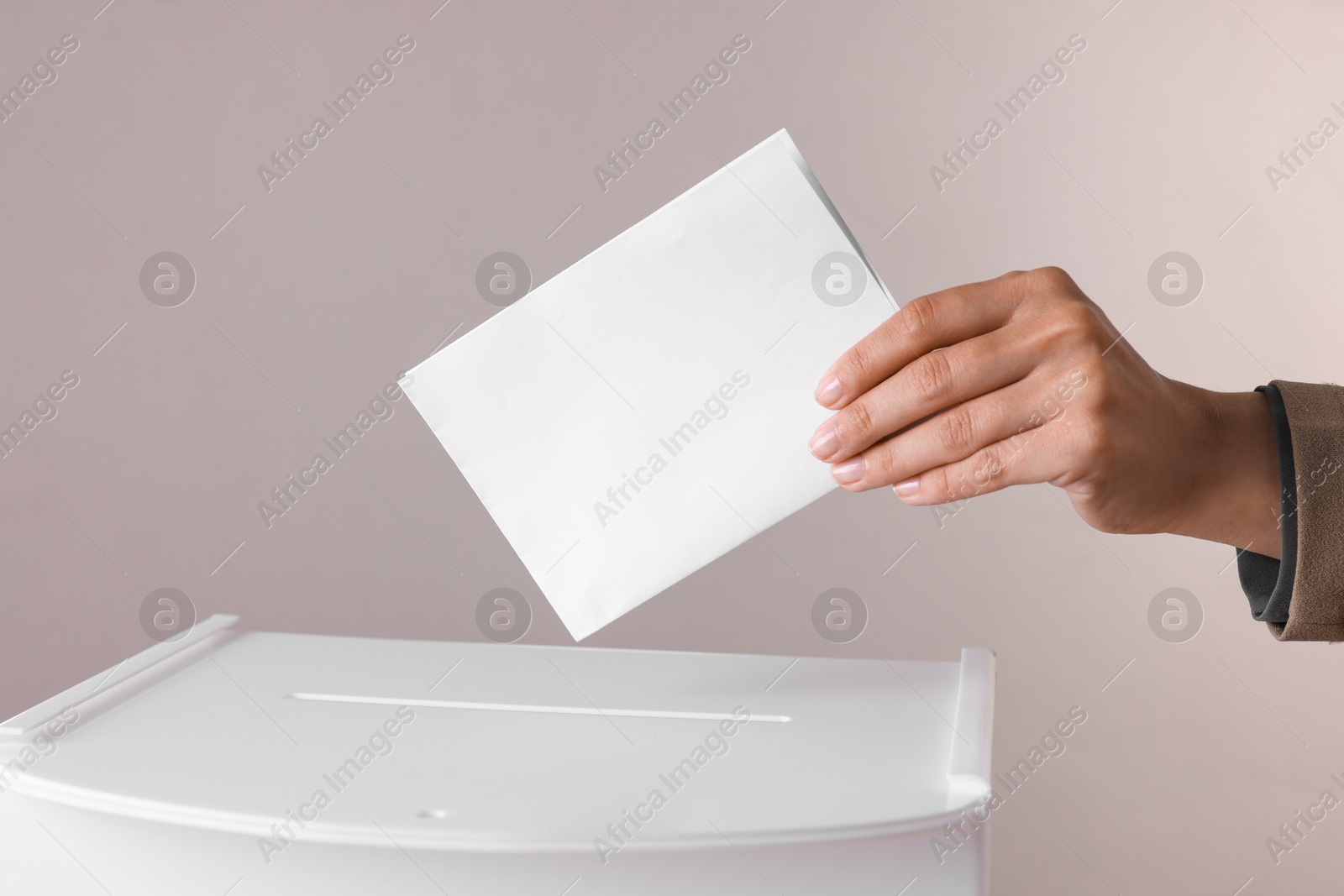 Photo of Woman putting her vote into ballot box against grey background, closeup