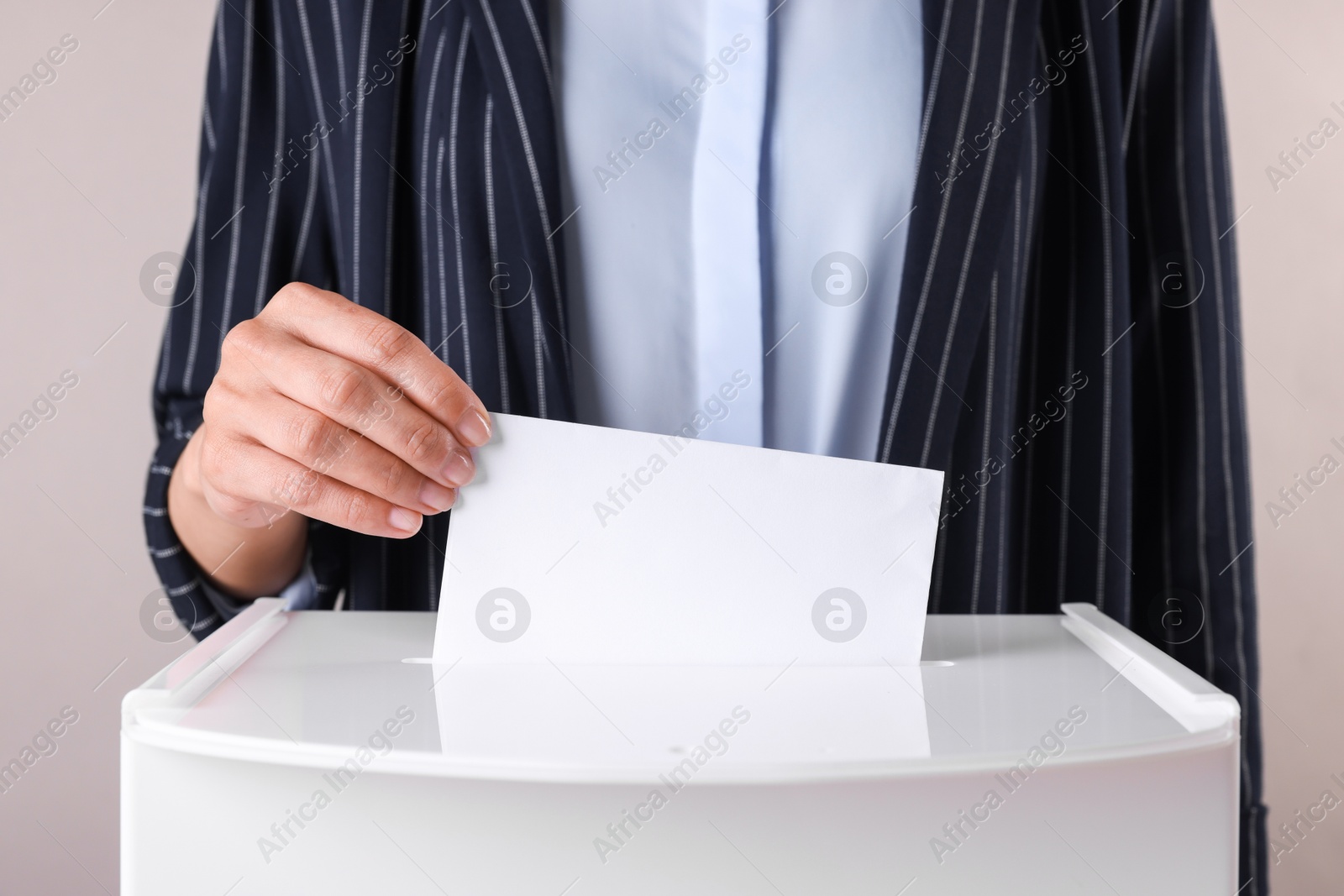 Photo of Woman putting her vote into ballot box against grey background, closeup