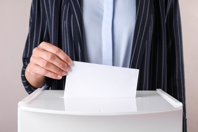 Photo of Woman putting her vote into ballot box against grey background, closeup