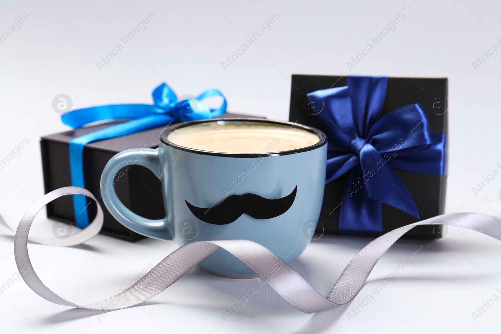 Photo of Happy Father's Day. Cup of coffee with funny moustache and gift boxes on light background