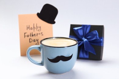 Photo of Greeting card with phrase Happy Father's Day, gift and cup of coffee on light background