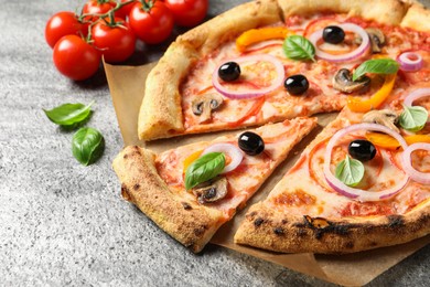 Photo of Cut delicious vegetarian pizza and tomatoes on grey table, closeup