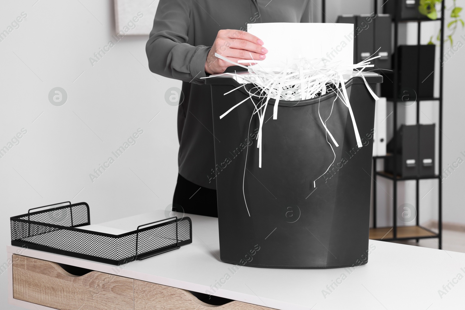 Photo of Woman destroying sheet of paper with shredder at white table in office, closeup