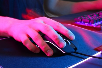 Photo of Gamer using modern wired computer mouse in neon lights at dark table, closeup