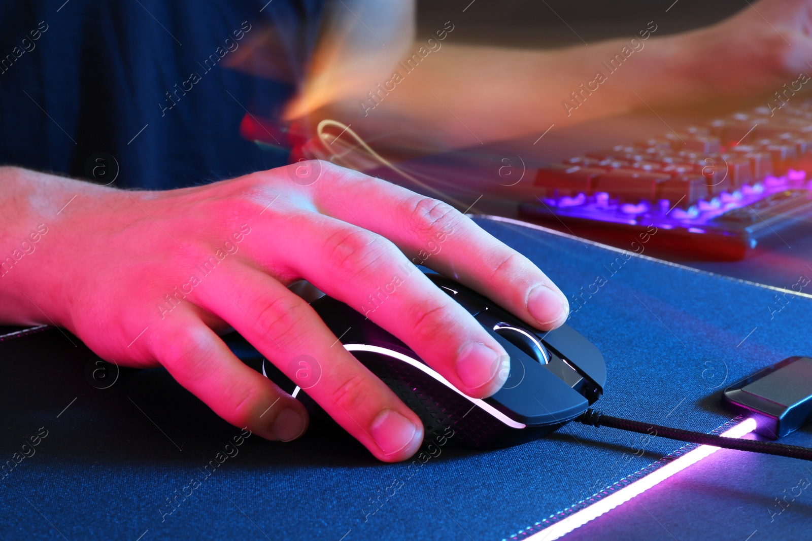 Photo of Gamer using modern wired computer mouse in neon lights at dark table, closeup