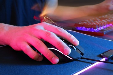 Photo of Gamer using modern wired computer mouse in neon lights at dark table, closeup