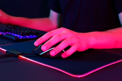 Photo of Gamer using modern wired computer mouse in neon lights at black table, closeup