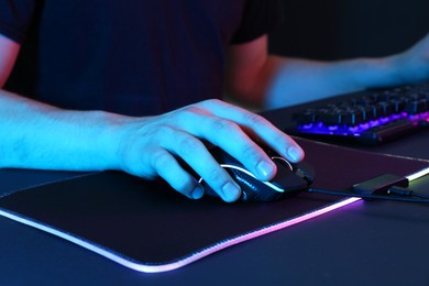 Photo of Gamer using modern wired computer mouse in neon lights at dark table, closeup