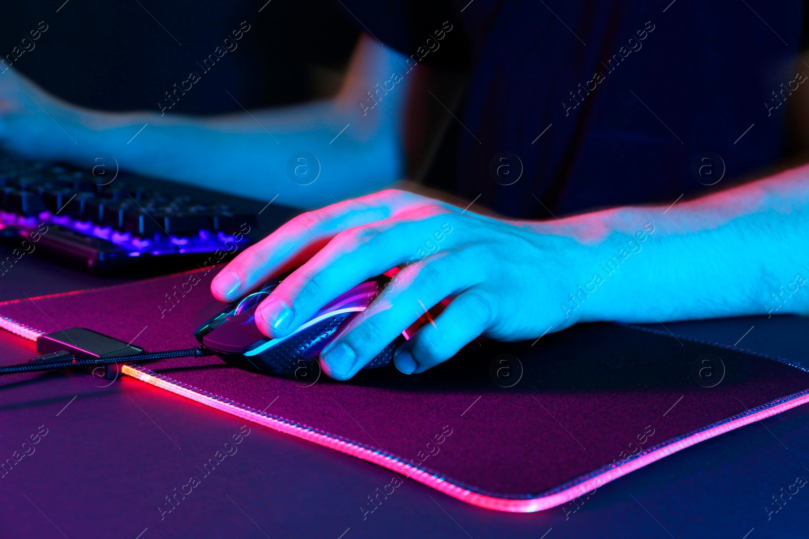 Photo of Gamer using modern wired computer mouse in neon lights at dark table, closeup