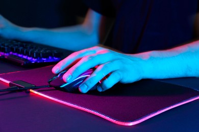 Photo of Gamer using modern wired computer mouse in neon lights at dark table, closeup