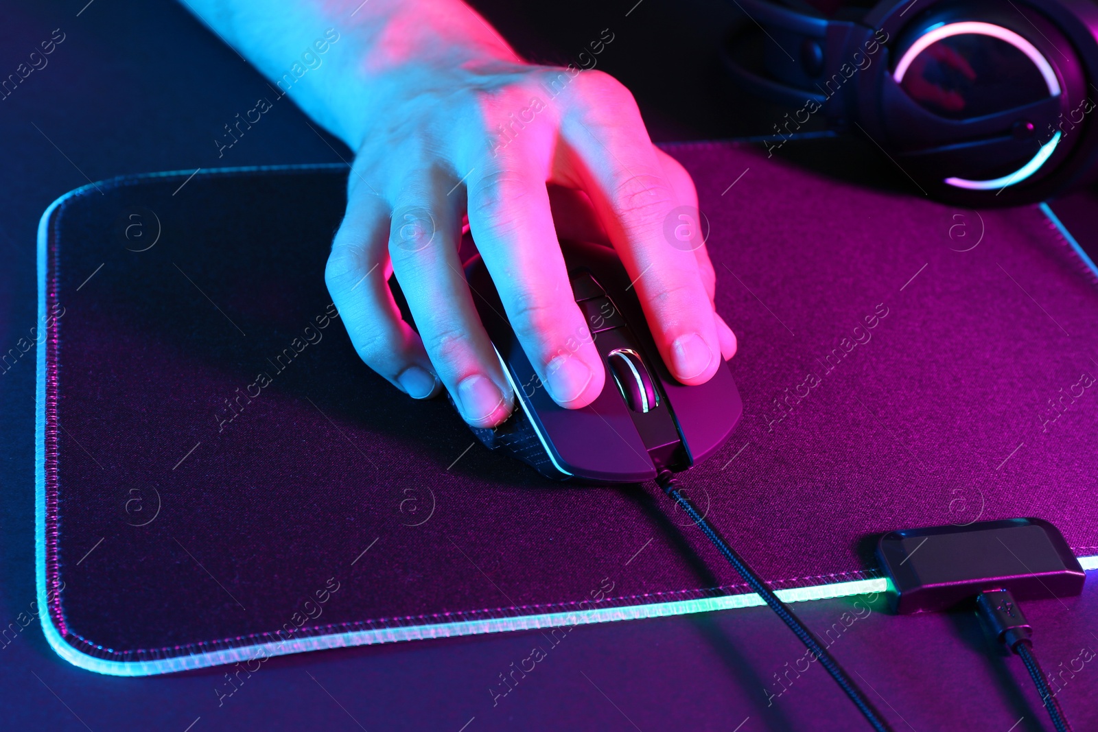 Photo of Gamer using modern wired computer mouse in neon lights at dark table, closeup