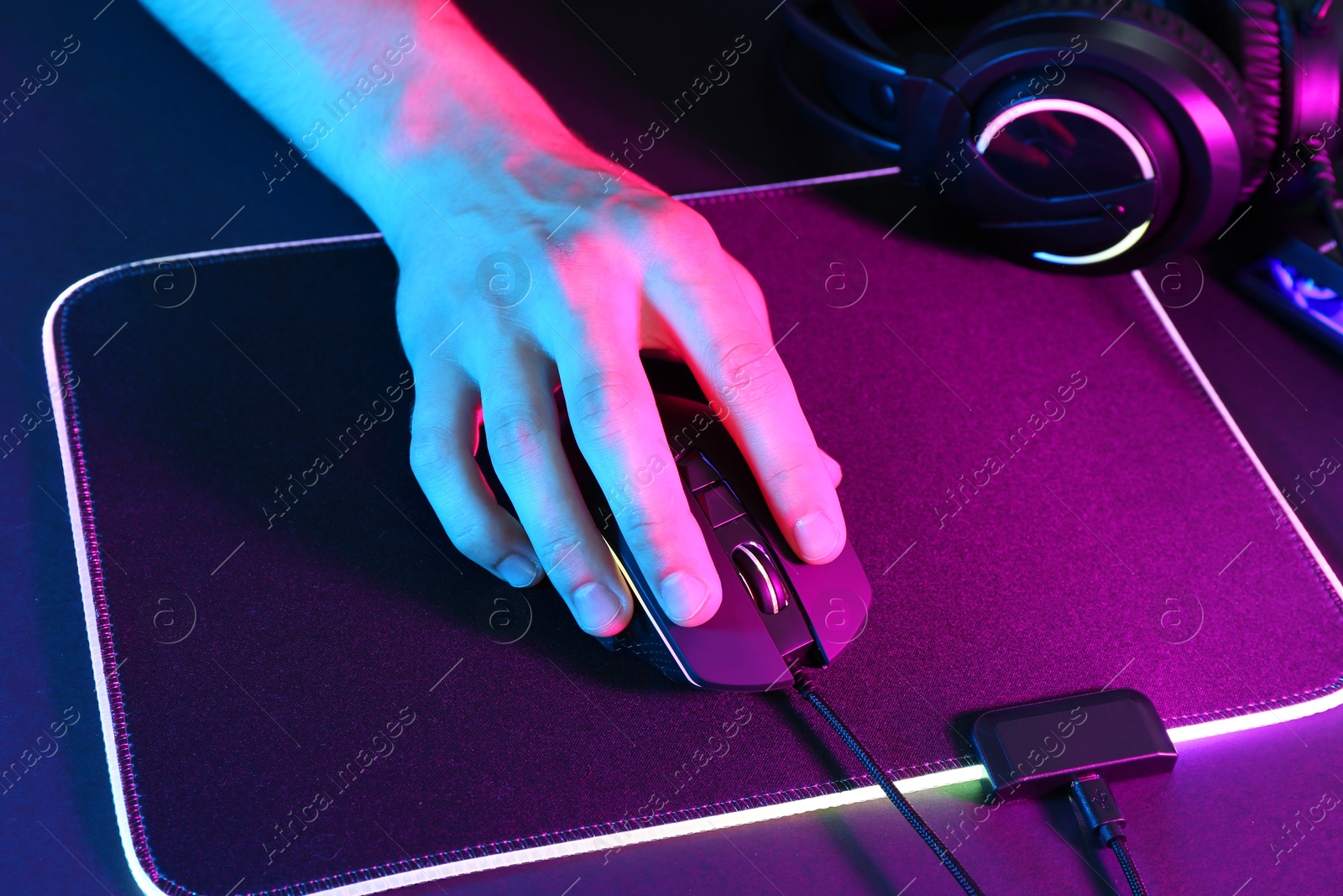 Photo of Gamer using modern wired computer mouse in neon lights at dark table, closeup