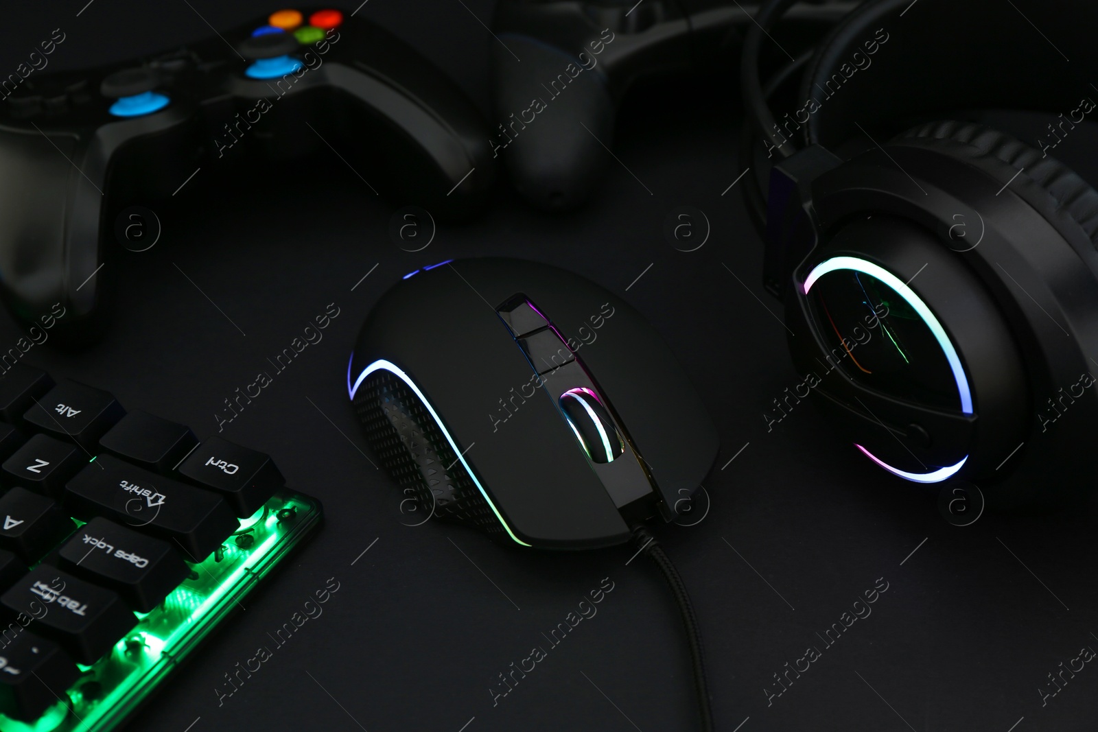 Photo of Computer mouse, headset, RGB keyboard and game controllers on black background, closeup