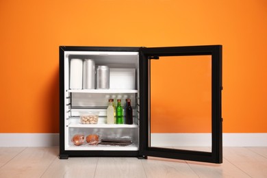 Mini refrigerator with different drinks and snacks near orange wall