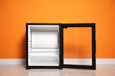 Empty modern mini refrigerator near orange wall