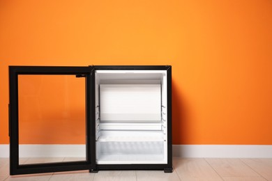 Photo of Empty modern mini refrigerator near orange wall