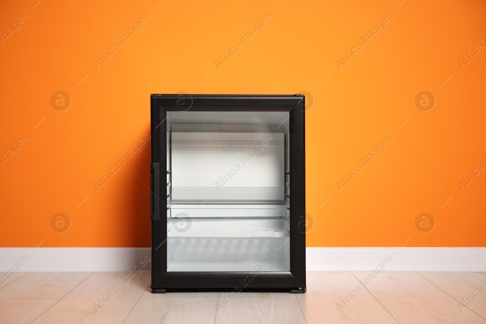 Photo of Empty modern mini refrigerator near orange wall