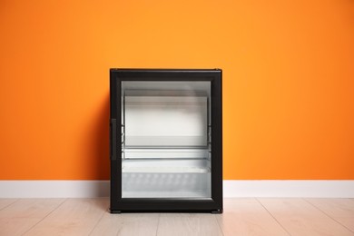 Empty modern mini refrigerator near orange wall