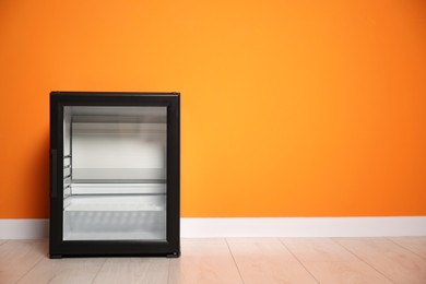 Empty modern mini refrigerator near orange wall, space for text