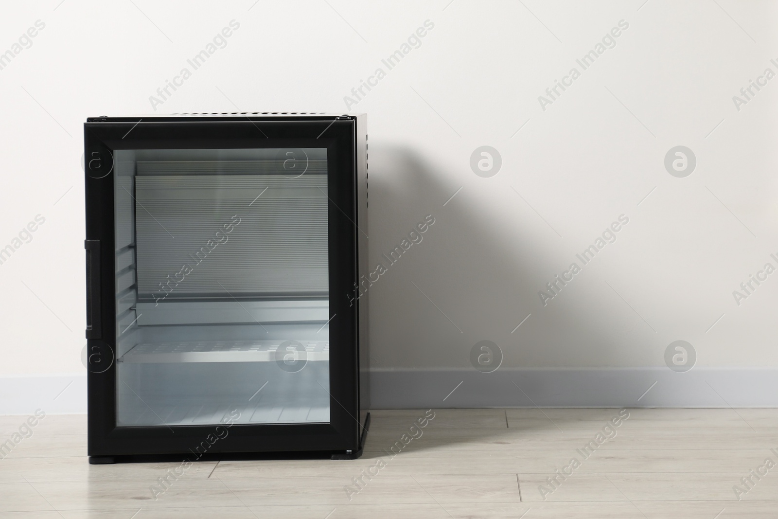 Photo of Empty modern mini refrigerator near white wall, space for text