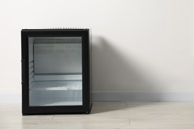 Empty modern mini refrigerator near white wall, space for text