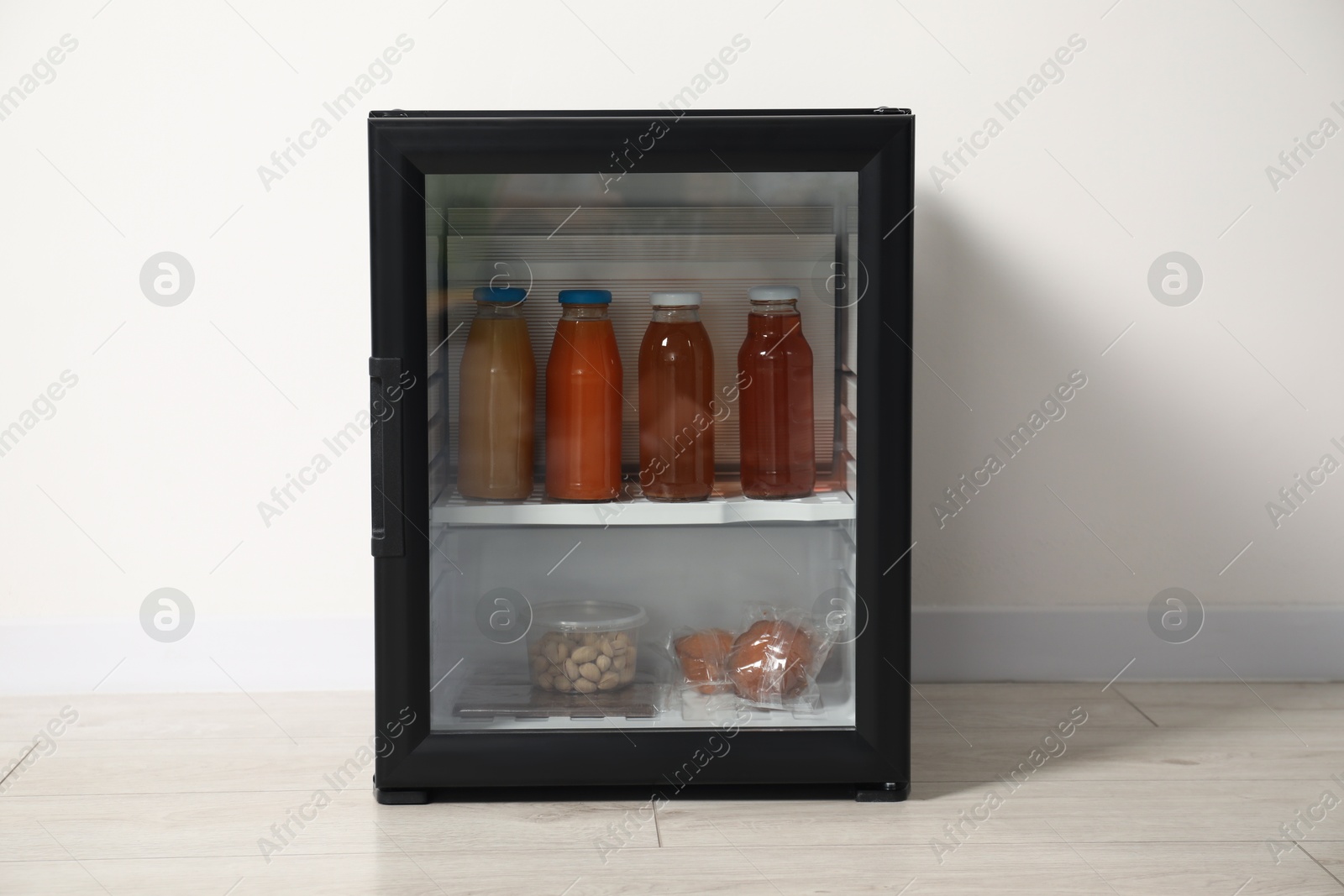 Photo of Mini refrigerator with different drinks and snacks near white wall