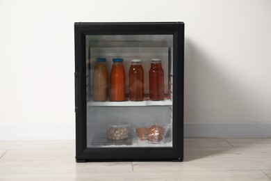 Mini refrigerator with different drinks and snacks near white wall