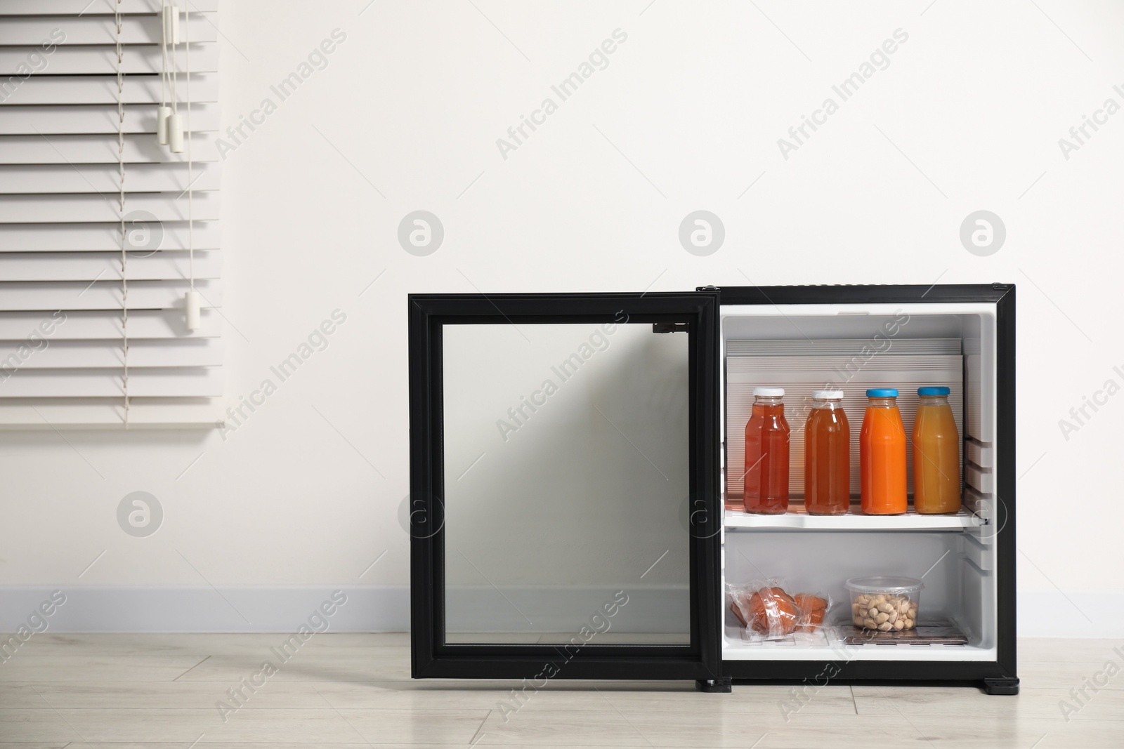 Photo of Mini refrigerator with different drinks and snacks near white wall