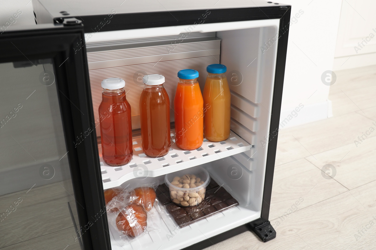 Photo of Mini refrigerator with different drinks and snacks near white wall