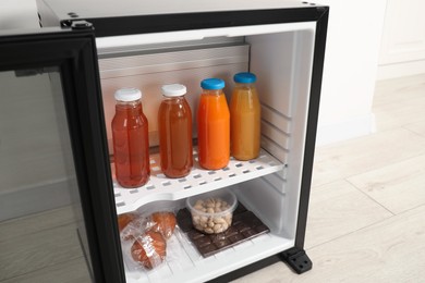 Photo of Mini refrigerator with different drinks and snacks near white wall