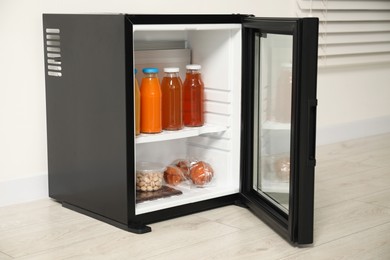 Mini refrigerator with different drinks and snacks near white wall