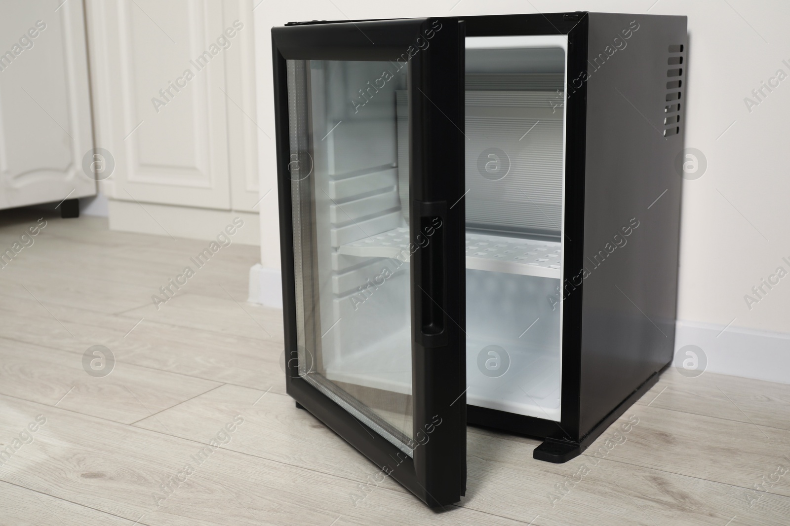 Photo of Empty modern mini refrigerator on floor indoors