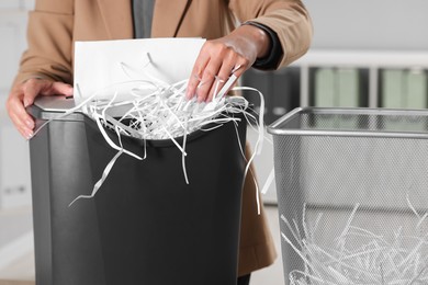 Photo of Woman destroying sheets of paper with shredder in office, closeup