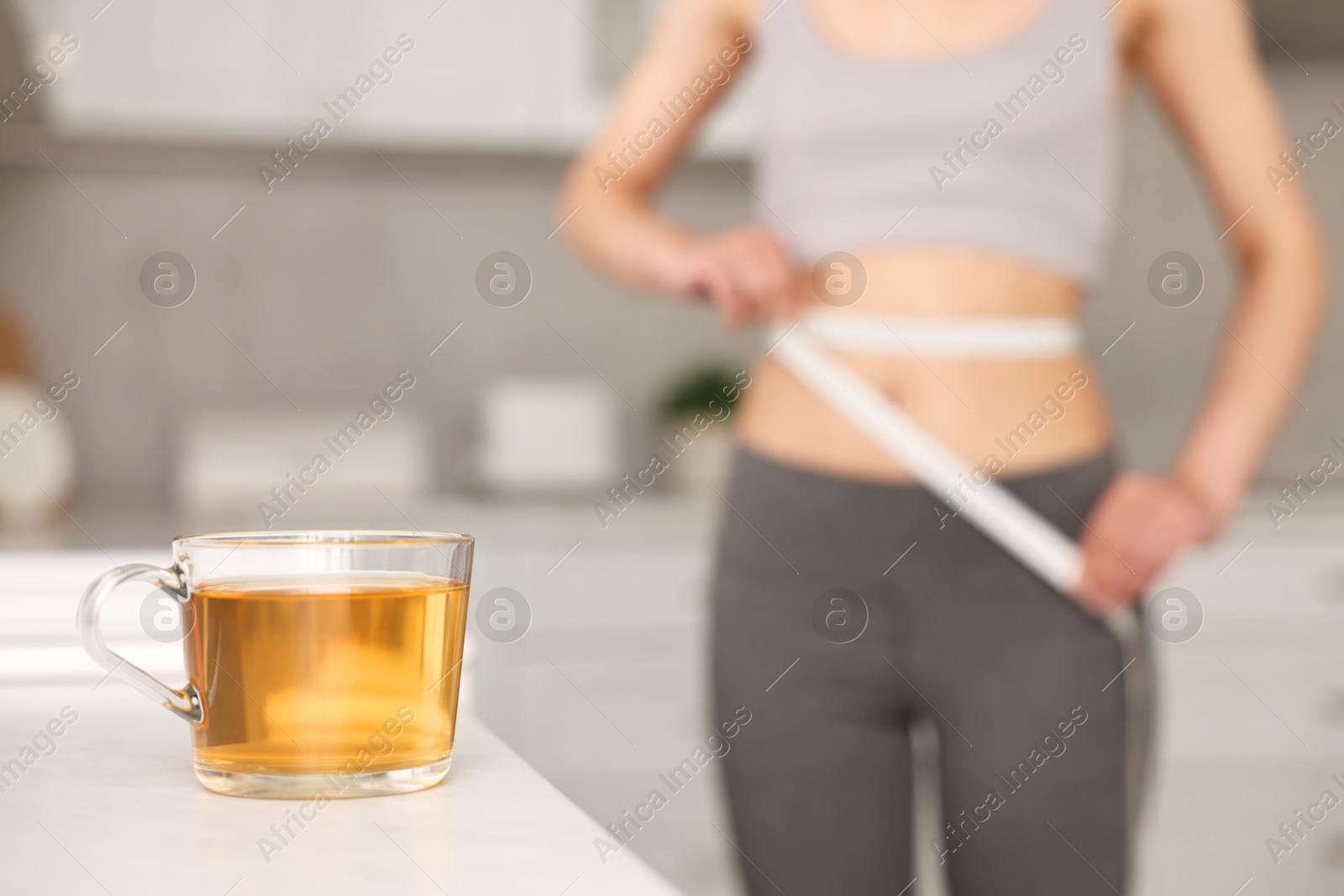 Photo of Weight loss concept. Woman with measuring tape indoors, focus on cup of diet tea on white table