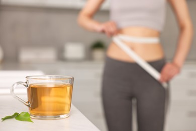 Photo of Weight loss concept. Woman with measuring tape indoors, focus on cup of diet tea on white table