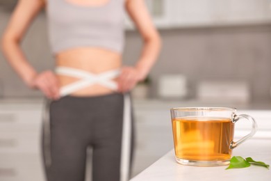 Photo of Weight loss concept. Woman with measuring tape indoors, focus on cup of diet tea on white table