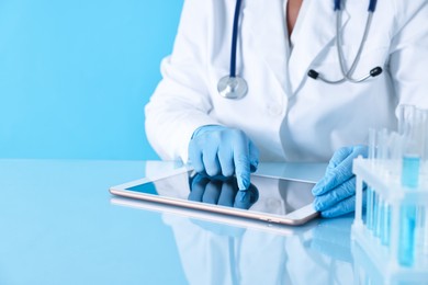 Photo of Doctor with tablet at table against light blue background, closeup view