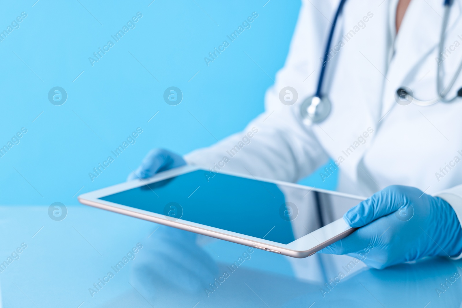 Photo of Doctor with tablet at table against light blue background, closeup view