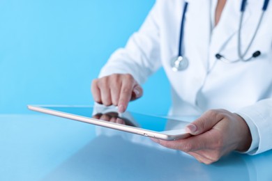 Photo of Doctor with tablet at table against light blue background, closeup view