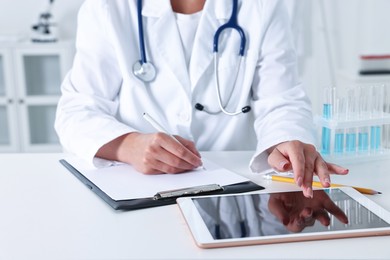 Doctor with tablet at table in clinic, closeup view