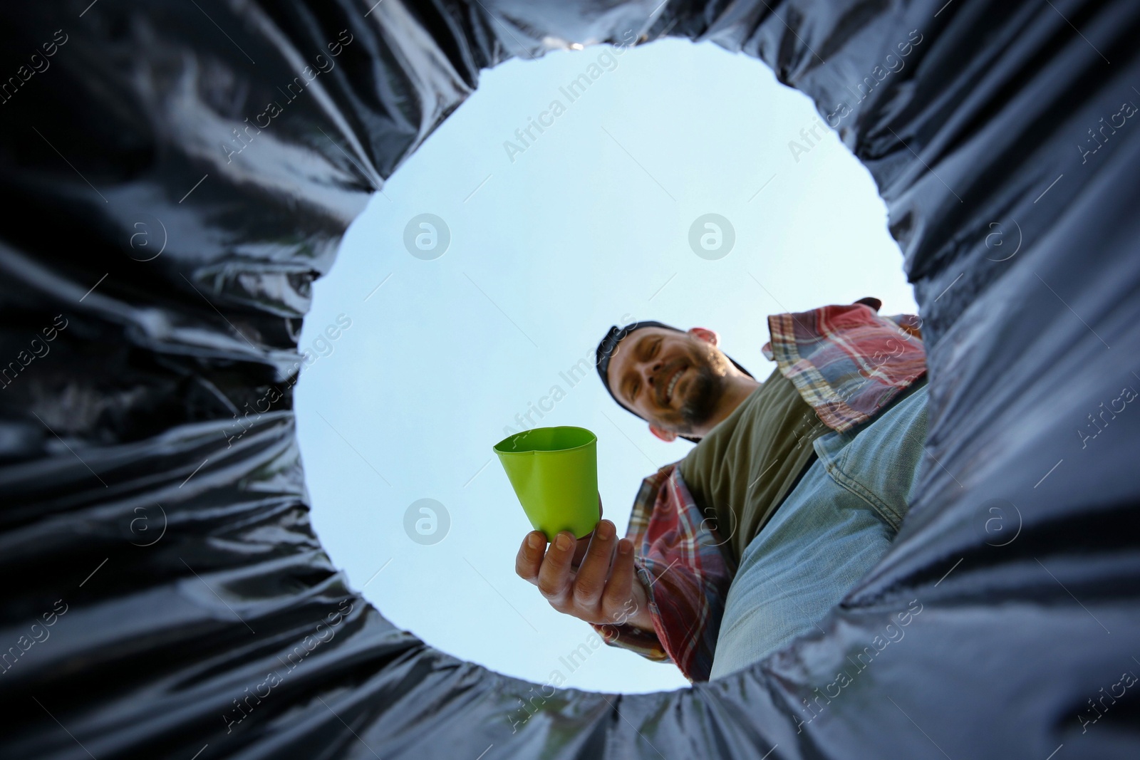 Photo of Man throwing garbage into trash bin outdoors, bottom view