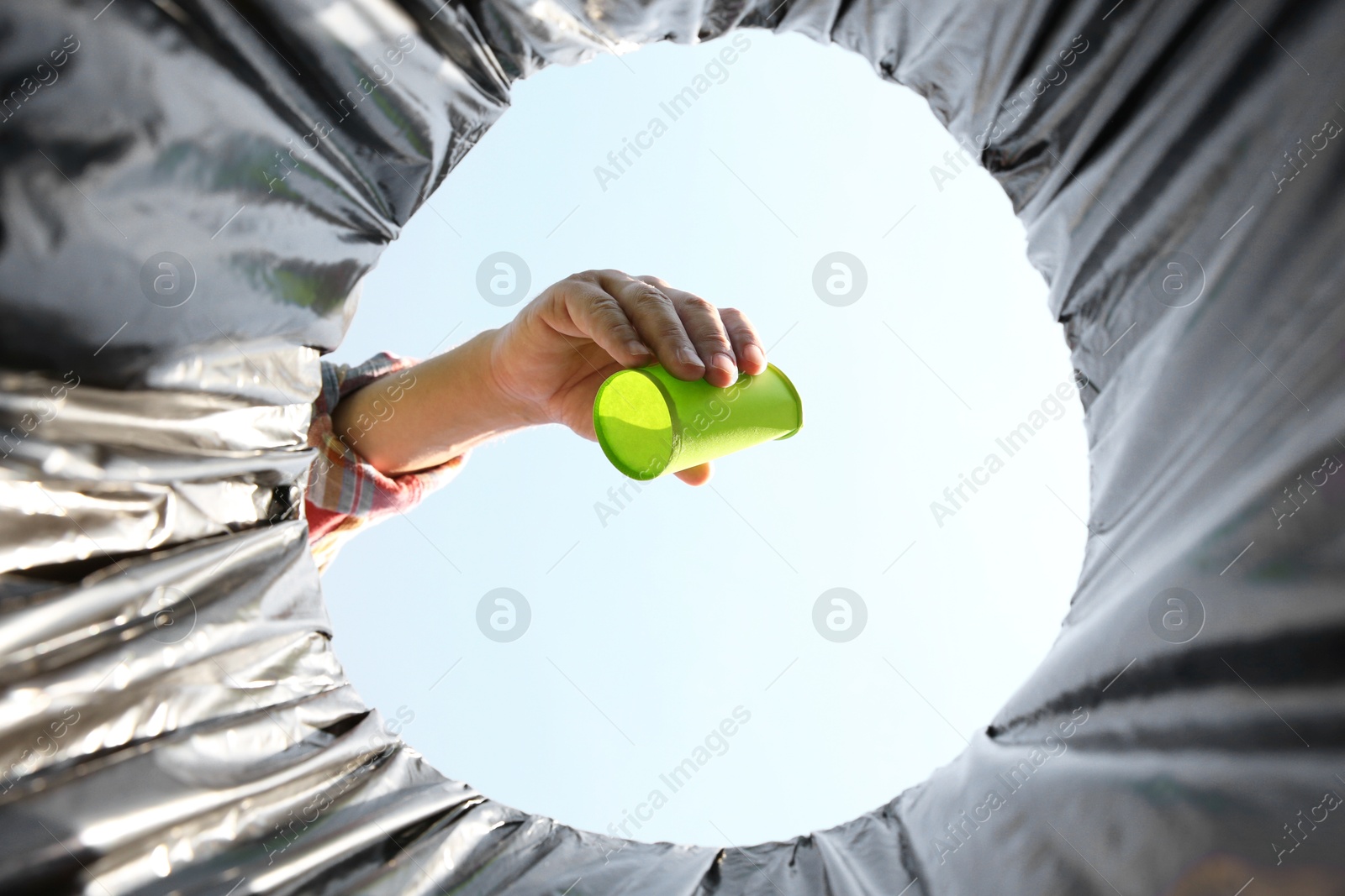 Photo of Man throwing garbage into trash bin outdoors, bottom view