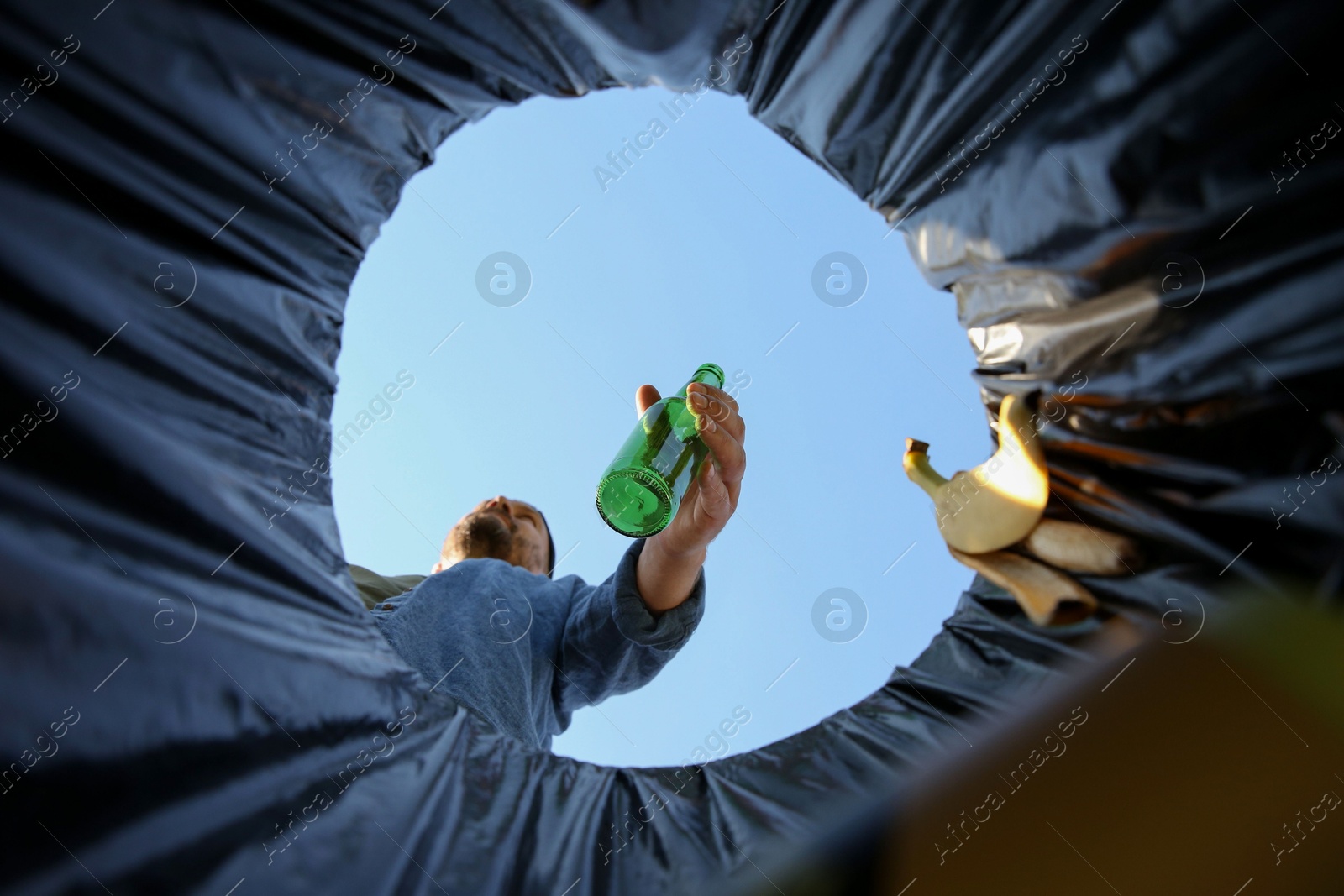 Photo of Man throwing glass bottle into garbage bin outdoors, bottom view