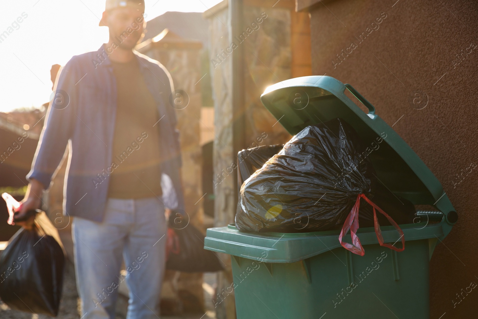 Photo of Man with trash bags full of garbage and bin outdoors, selective focus